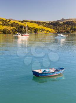 Old weathered blue rowing boat moored in Akaroa Harbor in New Zealand with other yachts in the background