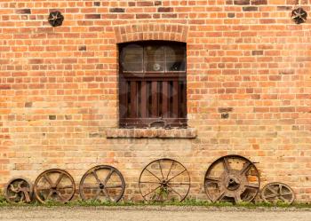 Old farming cartwheels leaning against aged brick of barn or farm building