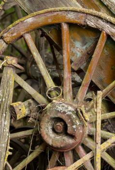 Old wooden cartwheel against a ruined wood cart or buggy in detailed close up