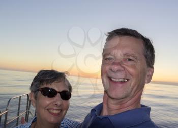 Selfie of middle aged couple on an ocean sunset cruise and leaning against the railings. Smiling and facing the camera.
