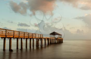 Long exposure image of Waimea pier at sunset blurs the ocean and bathes the structure in the warm glow of the setting sun. Taken on island of Kauai in Hawaiian islands
