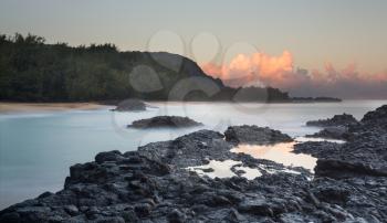 Rocks and rockpools lead into the blurred motion of the waves and ocean at Lumahai Beach in Kauai in Hawaiian islands