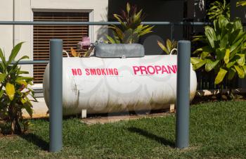 Large white propane storage tank behind protective pillars in landscaped garden by home or holiday resort