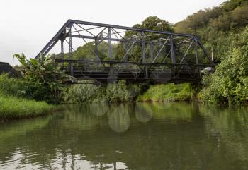 View of the old steel girder bridge over Hanalei river from a canoe floating down the wide stream under the road bridge