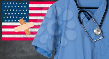 Blue doctor scrubs shirt and stethoscope hang empty in front of USA flag. Illustration of healthcare system problems with bandage stuck to flag