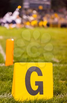 Yellow american football goal line marker at school field with the student athletes on the field
