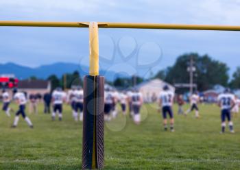 Yellow american football goal posts at school field with the student athletes on the field