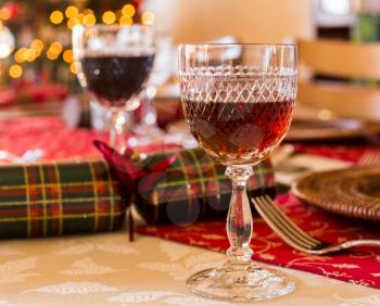 Christmas sherry in cut glass goblet on table set for Christmas lunch with crackers and decorated tree in background