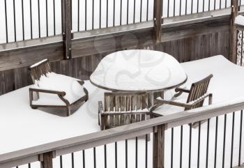 Very deep snow piles up in nice volcano shape on a wooden table and chairs on a tiered deck in backyard