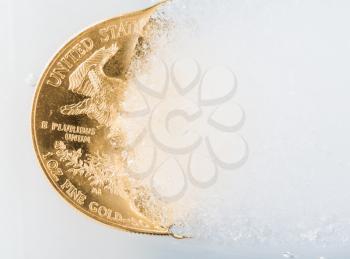 Gold eagle one ounce coin emerging from a frozen ice block to illustrate concept of gold coming out of deep freeze, pricing going to rise