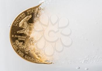 Gold eagle one ounce coin emerging from a frozen ice block to illustrate concept of gold coming out of deep freeze and price going to rise