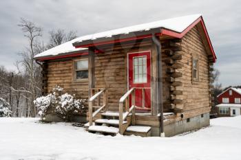Small log cabin on snowy winter day with steps leading up to red painted door.