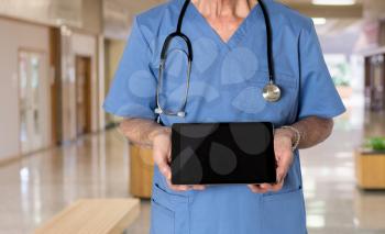 Senior male caucasian doctor with stethoscope in medical scrubs looking up and holding electronic tablet for message