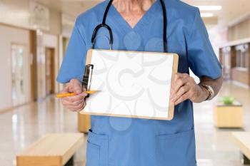 Senior male caucasian doctor with stethoscope in medical scrubs and holding clipboard for message with pencil for emphasis