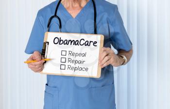Senior male caucasian doctor with stethoscope in medical scrubs and holding clipboard for Obamacare message with pencil for emphasis