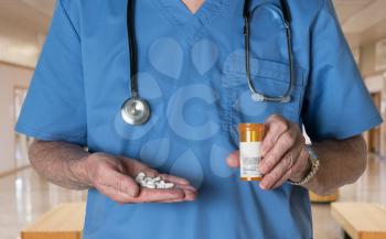 Senior male doctor with stethoscope in medical scrubs and holding bottle and tablets of generic white RX tablets to illustrate opioid epidemic