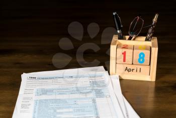 Wooden letters in calendar with Form 1040 income tax for 2016 showing tax day for filing is April 18 2017