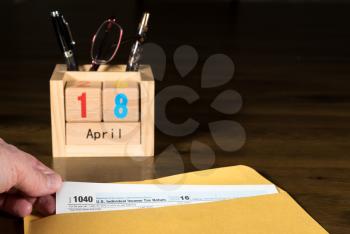 Wooden letters in calendar with Form 1040 income tax for 2016 showing tax day for filing is April 18 2017