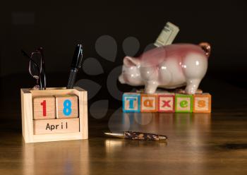 Wooden letters in calendar showing tax day for filing is April 18 2017 with savings piggy bank in background