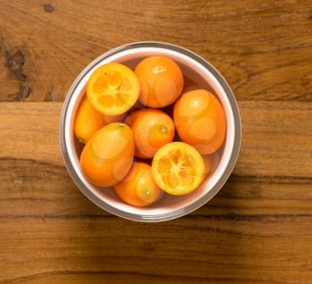 Aerial or top view of a white glass bowl of organic kumquat fruit with one sliced into two and sitting on old wood table surface