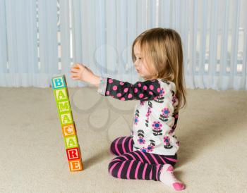 Young female toddler knocking over a tower of wooden blocks at home spelling Obamacare