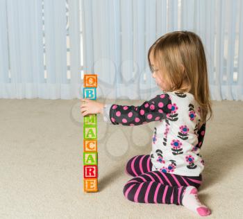 Young female toddler knocking down a tower of wooden blocks at home spelling Obamacare