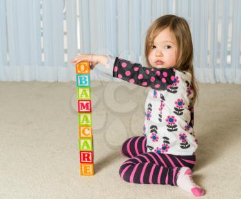 Young female toddler building a tower of wooden blocks at home spelling Obamacare