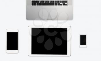 Modern computing equipment of smartphone, tablet, music player and laptop arranged on simple white desktop with copy space