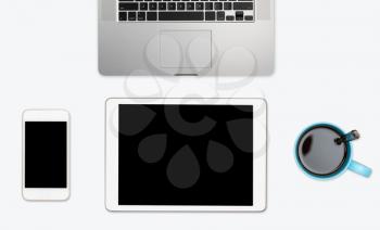 Modern computing equipment of smartphone, tablet and laptop with coffee cup arranged on simple white desktop with copy space
