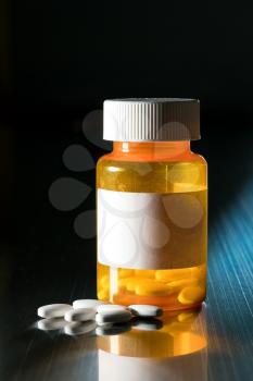 Prescription bottle with blank label for copy space and white pills or tablets on metal table for opioid epidemic illustration