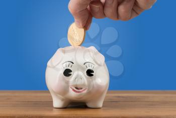 Pottery piggy bank on a table or shelf with a hand inserting a gold coin for savings or investment in the future