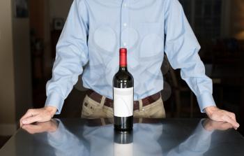 Senior caucasian man standing in kitchen with bottle of red wine with a blank label for copy space