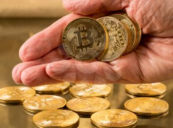 Stack of bit coins or bitcoin held in man's hand on gold background to illustrate blockchain and cyber currency