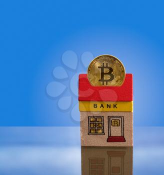 Toy brick bank building with bitcoins inside the windows and one coin emerging from roof into cyberspace. Illustration of the importance of modern techology to banking