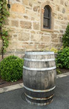 Wooden wine barrel standing by warm stone walls and window of ancient winery in Napa Valley California