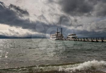 Cruise boats wait for passengers on Lake Tahoe in stormy spring day with snow on the distant Sierra Nevada Mountains