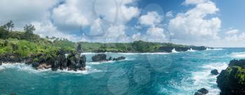 Broad panorama of vegetation covered rocks tower above the ocean at Waianapanapa State Park on the road to Hana in Maui, Hawaii