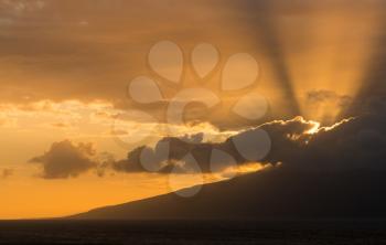 Sunset with sunbeams from behind clouds as the sun drops below the mountains of Molokai. Taken from north coast of Maui, Hawaii