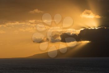 Sunset with sunbeams from behind clouds as the sun drops below the mountains of Molokai. Taken from north coast of Maui, Hawaii