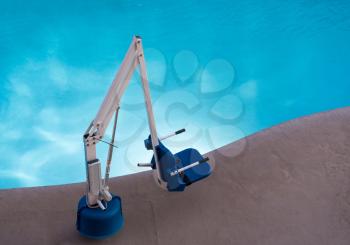 Disabled person pool lift or hoist meets ADA standards installed by swimming pool to lower people into water