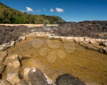 Rocks and rockpools lead into the ocean at Lumahai Beach in Kauai in Hawaiian islands