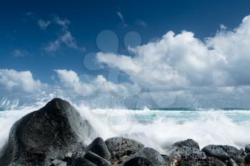 Cresting ocean waves crash against rocks of coastline showing trails of water in the surf