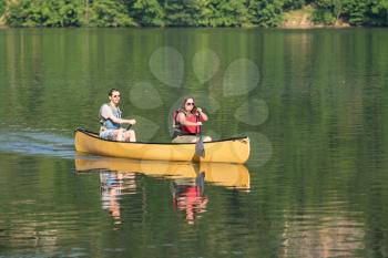 Male and female caucasian couple paddling a yellow canoe on a very calm morning on tree lined lake