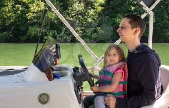 Father and young daughter driving a speedboat on a lake in summer while wearing a life jacket