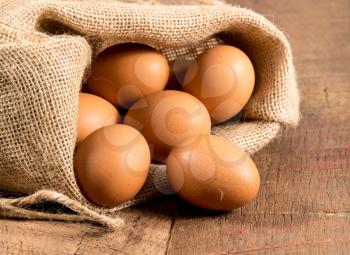Easter background with brown organic eggs arranged inside a burlap sack on rustic wooden table