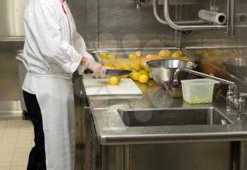 Chef cutting lemons in commercial stainless steel kitchen in restaurant