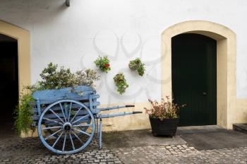 Blue wooden horse cart filled with flowers and plants by old white painted stone building with arches