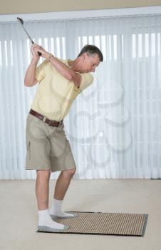 Senior caucasian man practicing his golf grip and swing on a mat in bedroom at home