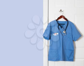 Blue medical scrubs uniform shirt hanging on a hook with I Vote sticker to illustrate healthcare issue in USA
