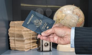 Senior executive hand holding US passport against blurred background of world globe and camera